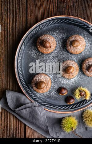 Muffins à base de purée de châtaignes et de cacao, recouverts de châtaignes pelées et cuites au four, saupoudrés de sucre en poudre sur fond de bois rustique Banque D'Images