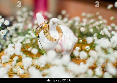 Gros plan sur une paire d'anneaux de mariage dorés une figurine de lapin blanche oreilles Banque D'Images