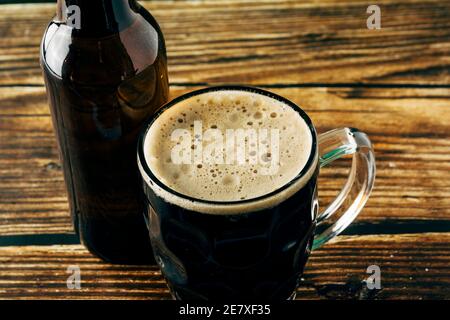 Gros plan de la mousse d'une bière foncée servie dans une tasse sur une table en bois. St. Patrick et Stout concept Banque D'Images