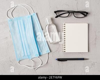 Masque médical bleu, désinfectant pour les mains et lunettes près du stylo et du carnet en papier avec espace pour copier. Protection contre le covid, la grippe et les infections virales. Banque D'Images