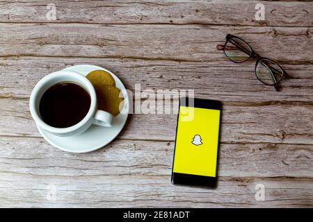 Un téléphone portable ou mobile posé sur un bois Table avec une application Snapchat ouvrant également un café et lunettes Banque D'Images