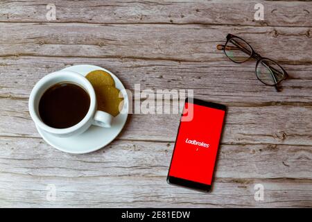 Un téléphone portable ou mobile posé sur un bois Table avec l'application Ladbrokes ouvrant également un café et lunettes Banque D'Images