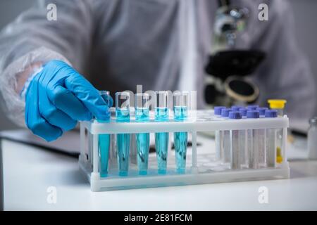 Gros plan des scientifiques mains dans des gants en latex bleu examine des échantillons de liquide chimique dans des tubes à essai en laboratoire scientifique. Recherche et développement. Laboratoire Banque D'Images