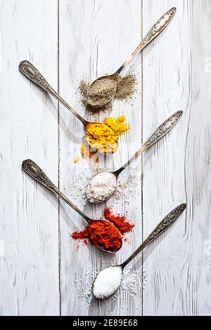 Différentes épices en cuillères vintage. Sel, curry, curcuma, poivre moulu, paprika moulu plat sur une table en bois clair Banque D'Images