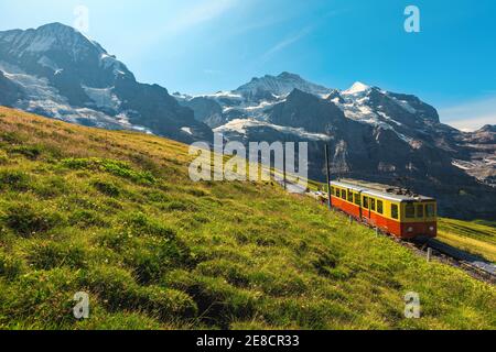 Train à crémaillère avec train touristique rétro-électrique rouge. Montagnes enneigées de la Jungfrau et train de voyageurs rouges sur la Jungfraujoch, Kleine Scheidegg, Grinde Banque D'Images