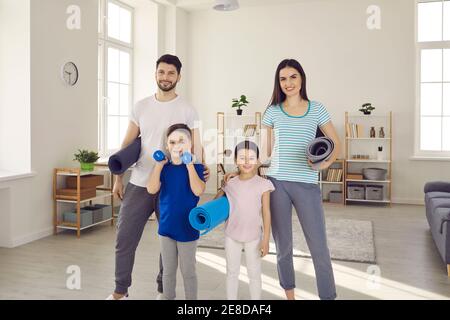 Portrait d'une jeune famille active avec des enfants tenant des tapis de sport et regardant l'appareil photo. Banque D'Images