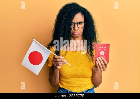 Femme afro-américaine d'âge moyen, portant le drapeau japonais et le passeport déprimé et s'inquiéter de la détresse, pleurant en colère et peur. Expression triste. Banque D'Images