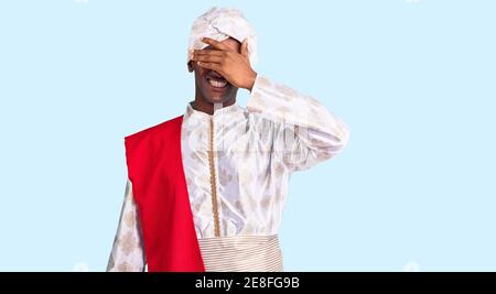 Homme beau africain portant des vêtements de saree de sherwani de tradition souriant et riant avec la main sur le visage couvrant les yeux pour la surprise. Concept aveugle. Banque D'Images