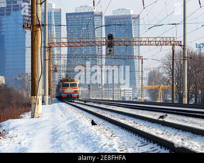 Un vieux train électrique se déplace sur des rails sur fond de paysage urbain de gratte-ciel lors d'une journée d'hiver ensoleillée. Banque D'Images