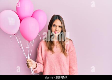 Jeune femme brune tenant des ballons roses pensant attitude et sobre expression en toute confiance Banque D'Images