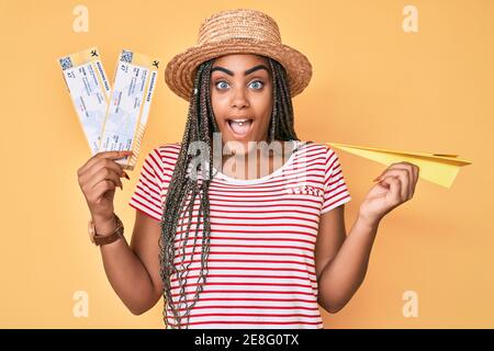 Jeune femme afro-américaine avec des tresses tenant un avion de papier et carte d'embarquement célébrant fou et émerveillé par le succès avec open les yeux hurlent ex Banque D'Images