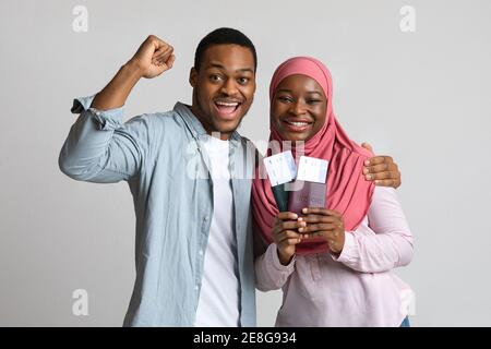 Couple enthousiaste tenant des billets de vol et des passeports sur fond gris Banque D'Images