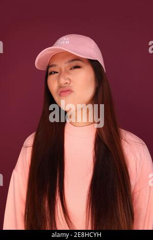 Portrait d'une jeune femme asiatique heureuse dans le studio portant des vêtements roses sur fond grenat Banque D'Images