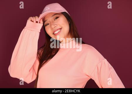 Portrait d'une jeune femme asiatique heureuse dans le studio portant des vêtements roses sur fond grenat Banque D'Images