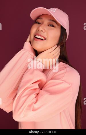 Portrait d'une jeune femme asiatique heureuse dans le studio portant des vêtements roses sur fond grenat Banque D'Images