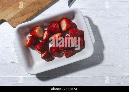 Vue de dessus des fraises mûres délicieuses sans calice entassé sur blanc plaque près de la planche à découper sur la barre de coupe Banque D'Images