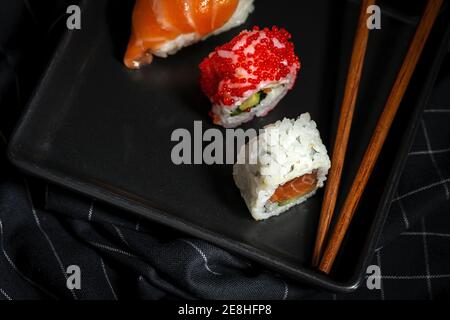 Vue de dessus composition de délicieux sushis frais divers et bambou baguettes servies sur un plateau noir sur un chiffon à carreaux Banque D'Images