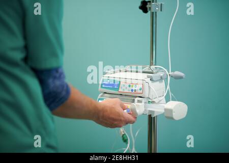 Vue latérale de la récolte médecin anonyme en contrôle d'uniforme médical IV sur pompe à perfusion moderne en salle d'opération Banque D'Images