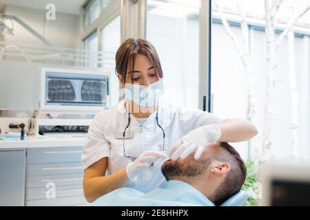 Dentiste féminin professionnel concentré en uniforme et masque de contrôle masculin les patients souffrent de la condition des dents lorsqu'ils travaillent dans une clinique dentaire moderne Banque D'Images