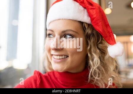 Femme pensive ravie en chapeau de père Noël et en col roulé rouge assis Dans le café et regarder les fenêtres pendant les vacances de Noël Banque D'Images