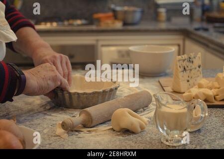 Crop anonyme chef avec pâte au-dessus de la table avec la cuisson plat et assortiment de fromages pendant la cuisson Banque D'Images