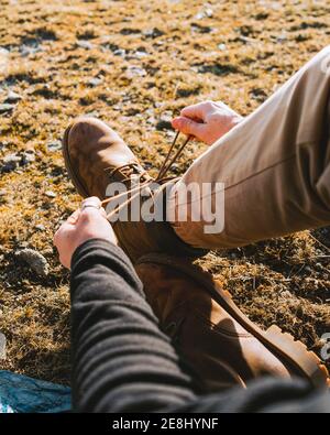 De dessus de crop anonyme homme randonneur dans une tenue élégante attacher les lacets des bottes en étant assis sur un sol herbeux jour ensoleillé Banque D'Images