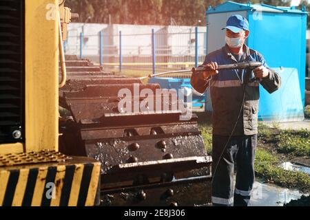 Le travailleur lave les chenilles du bulldozer à l'aide d'un pistolet à eau sous pression. Banque D'Images