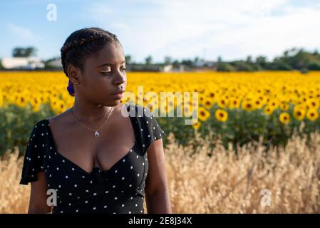 Femme afro-américaine vêque debout sur fond de floraison tournesols dans le champ et profiter de l'été dans la campagne Banque D'Images