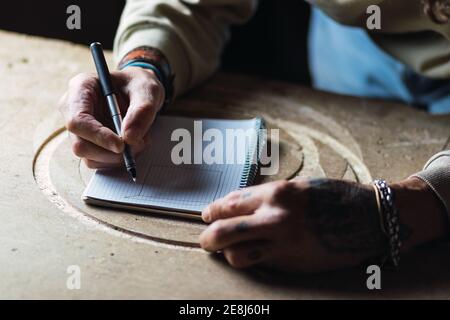Grand angle de recadrage anonyme homme menuisier dessin esquisse dans bloc-notes assis à l'établi en menuiserie Banque D'Images