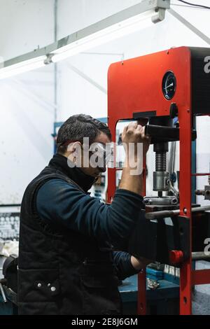 Vue latérale d'un mécanicien automobile masculin dans des lunettes de protection à l'aide de presse hydraulique lors de l'installation des roulements des véhicules Banque D'Images