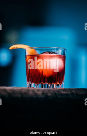 Verre de cocktail Negroni rafraîchissant au goût amer et à la glace garni de zeste d'orange et servi sur le bras de la table chambre sombre Banque D'Images