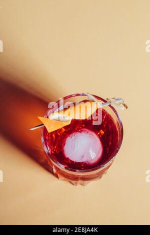 Verre de cocktail Negroni alcoolisé amer servi avec de la glace et pelage orange sur la surface légère Banque D'Images