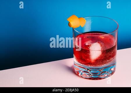 Verre de cocktail Negroni alcoolisé amer servi avec de la glace et pelage orange sur la surface légère Banque D'Images