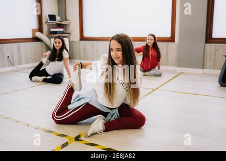 Danseurs féminins flexibles assis dans des fentes et s'étirant les jambes pendant préparation de la leçon dans un hall spacieux Banque D'Images