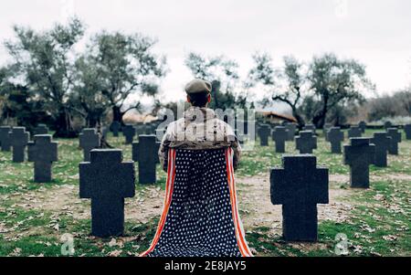 Vue arrière du corps du soldat en uniforme assis chaise avec drapeau américain tout en pleurant la mort des guerriers à cimetière Banque D'Images