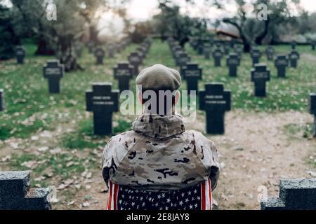 Vue arrière d'un soldat en uniforme assis sur une chaise avec Drapeau américain en pleurant la mort de guerriers au cimetière Banque D'Images