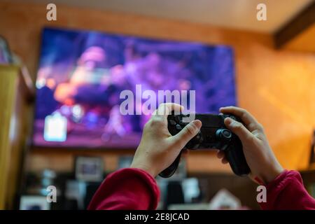 Rogner une personne anonyme avec un contrôleur jouant à des jeux vidéo dans la chambre Avec grand écran de télévision tout en vous amusant le week-end à la maison Banque D'Images