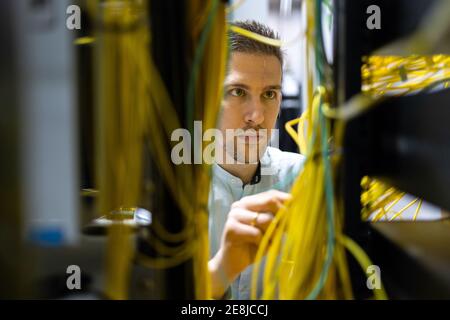 Spécialistes masculins concentrés travaillant avec des fils dans le serveur pendant la gestion réseau dans le centre de données Banque D'Images