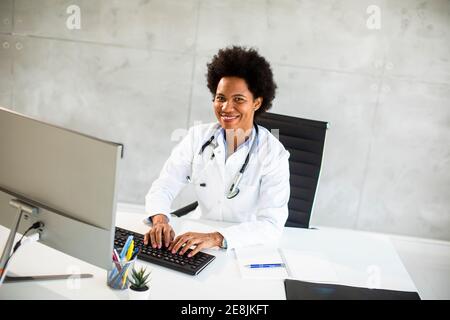 Femme afro-américaine médecin portant un manteau blanc avec stéthoscope assis derrière le bureau Banque D'Images