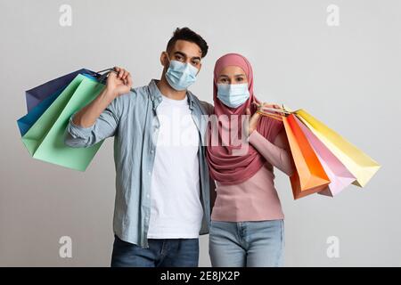 Portrait d'un heureux couple musulman portant des masques médicaux posant avec sacs à provisions Banque D'Images