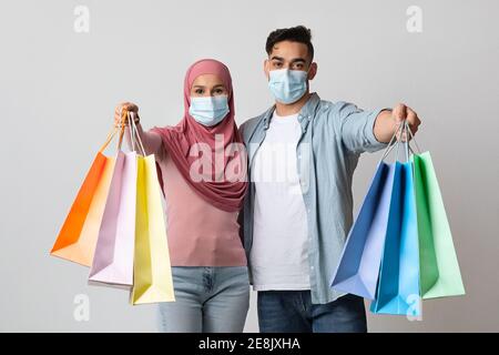Pandemic Shopping, couple musulman gai en masques médicaux protecteurs montrant des sacs d'achats Banque D'Images