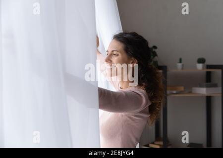 Bonne jeune belle femme caucasienne ouvrant les rideaux. Banque D'Images