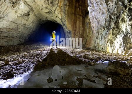 Femme en blouson jaune debout à l'intérieur d'une grotte, illuminé bu un contre-jour, des stalagmites fondus faits de glace à l'avant, Slovénie