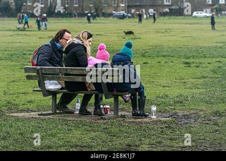 WIMBLEDON LONDRES, ROYAUME-UNI 31 JANVIER 2021. Une famille assise sur un banc . Malgré le temps froid et les températures glaciales, de nombreuses personnes marchent avec leurs chiens ou avec leurs familles et leurs amis sur Wimbledon Common lors du troisième confinement. Le gouvernement a conseillé aux gens de rester à la maison pour freiner la propagation de la nouvelle variante COVID-19 afin d'alléger la pression sur le crédit NHS: amer ghazzal/Alamy Live News Banque D'Images