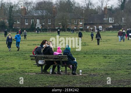 WIMBLEDON LONDRES, ROYAUME-UNI 31 JANVIER 2021. Une famille assise sur un banc. Malgré le temps froid et les températures glaciales, de nombreuses personnes marchent avec leurs chiens ou avec leurs familles et leurs amis sur Wimbledon Common lors du troisième confinement. Le gouvernement a conseillé aux gens de rester à la maison pour freiner la propagation de la nouvelle variante COVID-19 afin d'alléger la pression sur le crédit NHS: amer ghazzal/Alamy Live News Banque D'Images