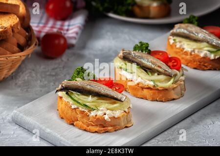 Sandwich au sprat fumé - poisson, concombre frais et tomate. Croque-monsieur sur des tranches de pain grillées Banque D'Images