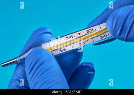 la personne en gants médicaux tient un thermomètre au mercure qui indique une température de 37. concept de fièvre Banque D'Images