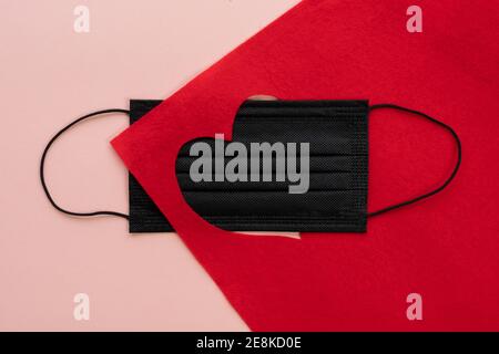 Composition pour la Saint-Valentin 14 février. Masque médical noir visage sortant rouge coupé forme de coeur sur fond rouge texturé vif rouge rose. Accueil Banque D'Images