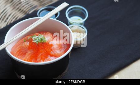 Vue de dessus et foyer au saumon avec riz japonais ou Saumon Ikura Don dans un plat en papier du restaurant de livraison Nappes noires Banque D'Images