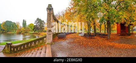 Panorama sur des bancs vides sous de vieux châtaigniers et anciennes colonnes avec des feuilles rouges et orange tombées dans le Parc de la ville aux couleurs de l'automne dans la rai Banque D'Images